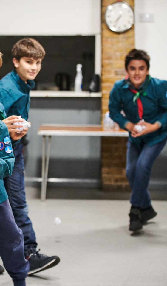 Scouts in teal shirts and neckerchiefs charging across their meeting hall throwing paper snowballs